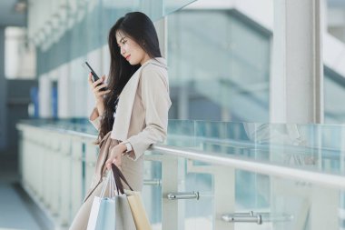 Asyalı iş kadını elinde dizüstü bilgisayarla telefonda yürüyor.