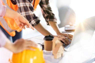 Genç bir mühendis bir proje evinin inşaat planını tartışıyor ve masasında bir dizüstü bilgisayar var..