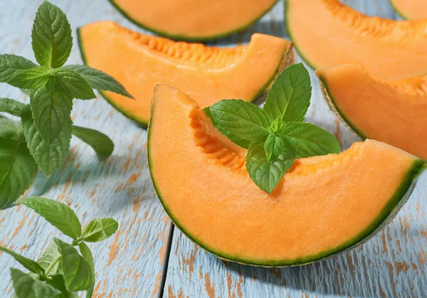 Sliced japanese melon, honey melon or cantaloupe melon and fresh mint on a wooden table.