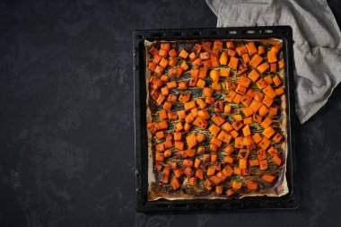 Baked pumpkin cut in small pieces on a dark baking sheet copy space for text. Homemade roasted butternut squash.