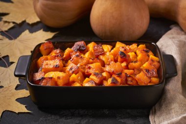 Oven baked pumpkin cubes  in a ceramic bowl, on a black stone table.