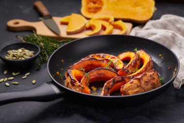 Organic roasted butternut squash in a pan on a black stone table.