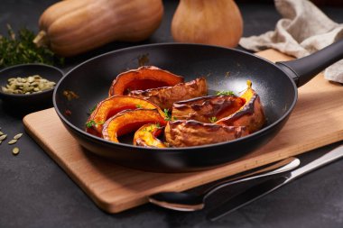 Organic roasted butternut squash in a pan on a black stone table.