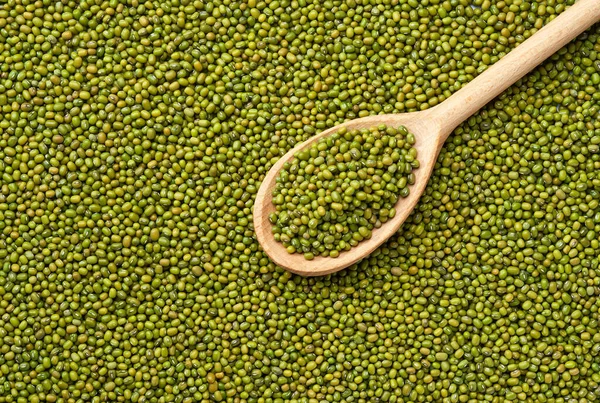wooden spoon with green mung beans on a close-up texture of raw mung beans