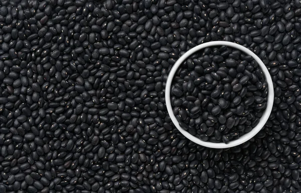 ceramic bowl with black beans (Urad dal, black gram, vigna mungo) on a close-up texture of raw black beans.