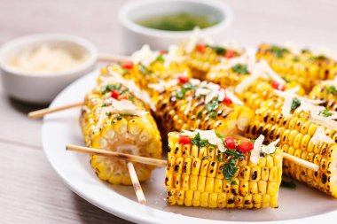 Grilled corn on cob sprinkled with cilantro and grated parmesan in a white dish on a table, close up.