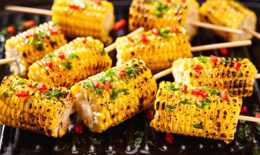 Traditional street food grilled corn cob with chilli pepper and cilantro on stick. Corn grilled with herbs. Ideas for barbecues and grill parties.