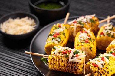 Plate with grilled corn on cob sprinkled with cilantro and grated parmesan  on dark background.