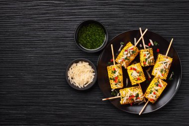 Grilled corn on cob sprinkled with cilantro and grated parmesan in a black dish on a table, copy space for text.