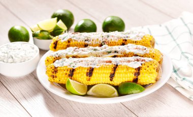 Elotes, grilled mexican street corn, roasted cobs are covered in creamy mayonnaise, seasoned with chili powder and cilantro and  lime, selective focus.