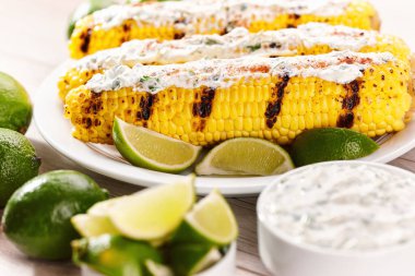 Elote on a white plate, grilled mexican street corn, roasted cobs are slathered in sour cream based sauce, seasoned with chili powder and sprinkled with cilantro.  vegan dinner or snack.