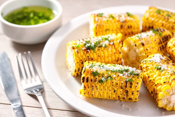 Grilled ripe corn with salt and cilantro.Summer vegan dinner or snack. grilled corn with salt and oil on a white plate close-up.