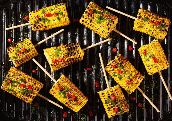 Traditional street food grilled corn cob with chilli pepper and cilantro on stick, top view. Ideas for barbecues and grill parties.