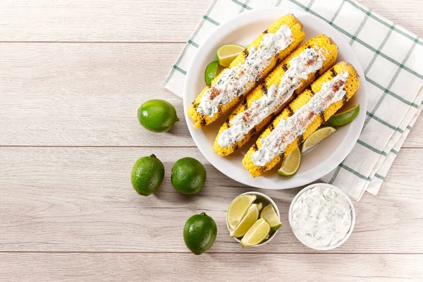 Flat-lay concept of grilled sweet corn with lime and sauce over white table, top view. Vegetarian, healthy, clean eating. Summer vegan dinner or snack.