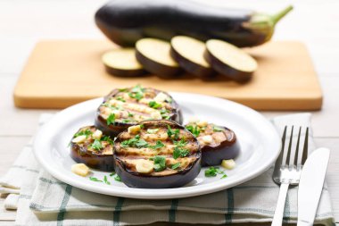 homemade eggplant salad with parsley and garlic on a white table. whole eggplant background.  Vegan lunch.