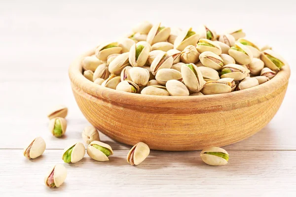 Pistachios in wooden bowl on white table, close-up. Bowl with pistachios on a wooden table.
