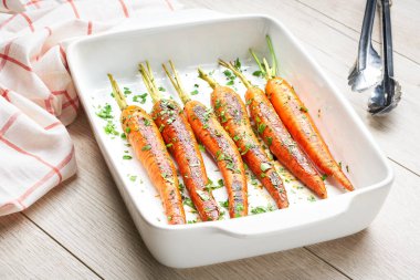 Tahta bir masada seramik formda taze maydanozlu kızarmış havuç. Sağlıklı kök sebze kavramı.