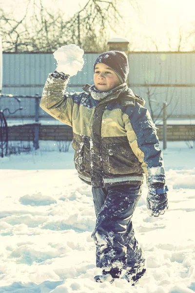 Chłopiec spacerujący po śniegu. Dziecko w zimowych ubraniach bawiące się śniegiem. Chłopiec robi śnieżną kulę na zewnątrz. Chłopiec grający w śnieżki w zimowym parku. Świąteczna zabawa. stonowana — Zdjęcie stockowe