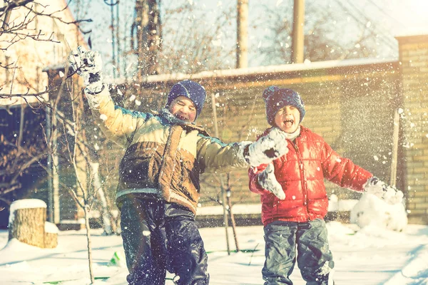 Dwóch chłopców bawi się śniegiem. Szczęśliwego dzieciństwa. Bracia na spacerze. Dwoje dzieci bawiących się śniegiem. stonowana — Zdjęcie stockowe