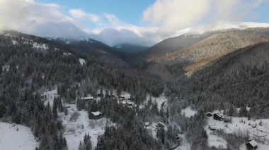 Soğuk dağlarda karla kaplı ormanlar arasında küçük kır evleri olan hava manzarası.