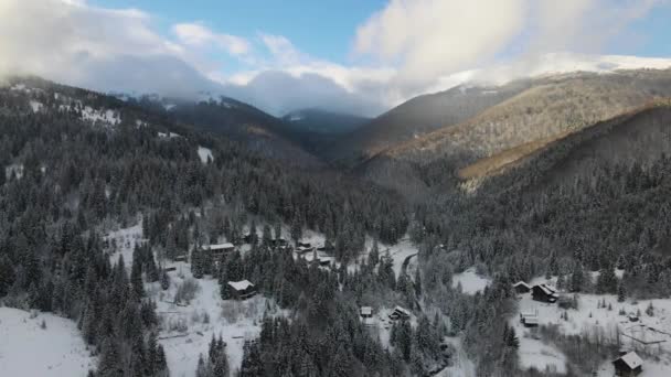 Letecká zimní krajina s malými venkovskými domy mezi zasněženými lesy v chladných horách. — Stock video