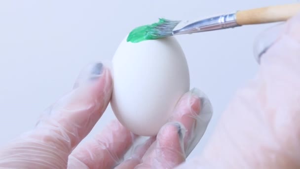 Κοντινό πλάνο ενός ατόμου που βάφει πασχαλινά αυγά με ένα ειδικό πινέλο. Ένα κορίτσι ζωγραφίζει ένα πασχαλινό αυγό πράσινο και άσπρο. Προετοιμασία για το Πάσχα. Λευκό τραπέζι, κοντινό. — Αρχείο Βίντεο
