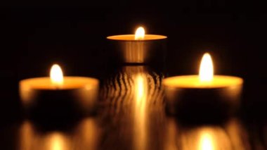 Mum karanlıkta titreşir. Beyaz yuvarlak bir mum koyu bir arka planda yanar. Yuvarlak mumlar yanar ve söner. Üzüntü. Romantizm. Neşe. 4K video