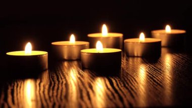 Mum karanlıkta titreşir. Beyaz yuvarlak bir mum koyu bir arka planda yanar. Yuvarlak mumlar yanar ve söner. Üzüntü. Romantizm. Neşe. 4K video