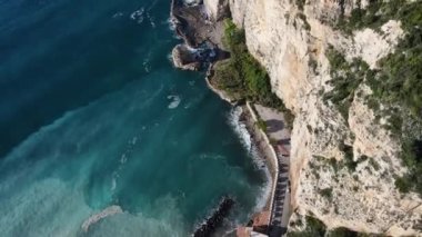 Dalgaların yukarıdan görünüşü mavi bir okyanusta kayalara çarpıyor. Deniz dalgaları güzel sahil manzaralı insansız hava aracı. Kuşların bakış açısı okyanus dalgalarının yukarıdan kayalıklara çarpmasını gösteriyor..