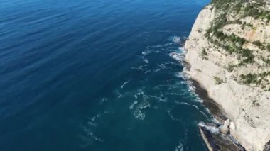 Dalgaların yukarıdan görünüşü mavi bir okyanusta kayalara çarpıyor. Deniz dalgaları güzel sahil manzaralı insansız hava aracı. Kuşların bakış açısı okyanus dalgalarının yukarıdan kayalıklara çarpmasını gösteriyor..