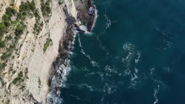Dalgaların yukarıdan görünüşü mavi bir okyanusta kayalara çarpıyor. Deniz dalgaları güzel sahil manzaralı insansız hava aracı. Kuşların bakış açısı okyanus dalgalarının yukarıdan kayalıklara çarpmasını gösteriyor..