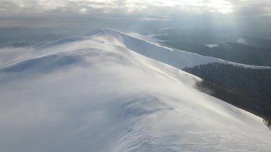Dağ tepelerinin üzerinden bulutların arasından uç. Sisli sıradağlar, çayırlar ve kış mevsiminde karla kaplı tepeler üzerinde inanılmaz bir uçuş. Gymba Dağı, Ukrayna Karpatları. 4k hava görüntüsü.