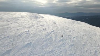 İki snowboardcu karla kaplı bir dağdan iniyor. İHA, alçalan snowboardcuların üzerinde uçuyor. Havadan çekim 4K video, üst görünüm.