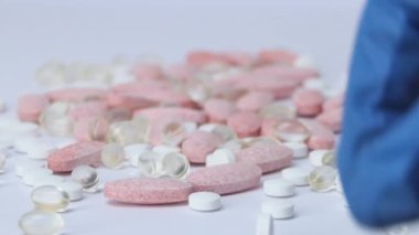 Bir tıp çalışanının eli hapları seçer. Bir adamın elindeki vitaminler, tıbbi eldivenli bir adam beyaz arka plandaki haplara bakar..