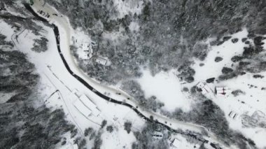 Karla kaplı bir ormanın havadan çekilmiş fotoğrafı. Karla kaplı tepelerin kış manzarası. Nefes kesici doğal manzara, donmuş orman ve karanlık dağ nehri..