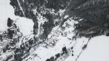 4K insansız hava aracı uçağını kayak merkezi köyüne götürüyoruz. Soğuk dağlarda karla kaplı ormanlar arasında küçük köy evleri olan havadan kış manzarası.