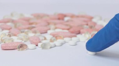 Bir tıp çalışanının eli hapları seçer. Bir adamın elindeki vitaminler, tıbbi eldivenli bir adam beyaz arka plandaki haplara bakar..