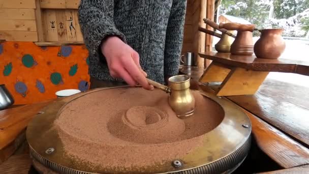 뜨거운 모래 위에 구리로 된 천장에 터키식 커피를 준비하는 것은 오래 된 터키식 커피 양조 방법이다. 한 남자가 겨울 산을 배경으로 커피를 마십니다. — 비디오
