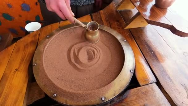 Sıcak kumda Türk kahvesi hazırlamak, eski bir Türk usulü kahve yapma yöntemidir. Bir adam, kış dağlarının arka planında kahve yapar.. — Stok video