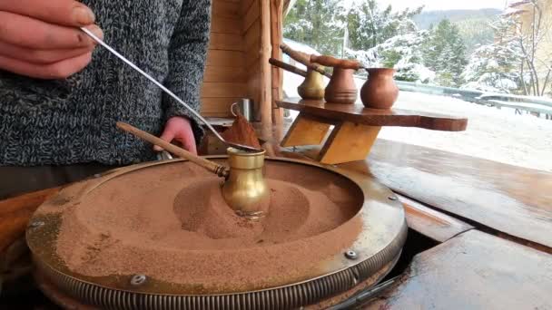 Готувати турецьку каву в мідному стейві на гарячому піску - це старий турецький спосіб приготування кавового напою. Чоловік заварює каву на тлі зимових гір.. — стокове відео