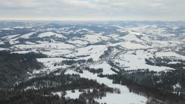 Paesaggio invernale aereo con piccole case rurali tra la foresta innevata in montagne fredde. — Video Stock