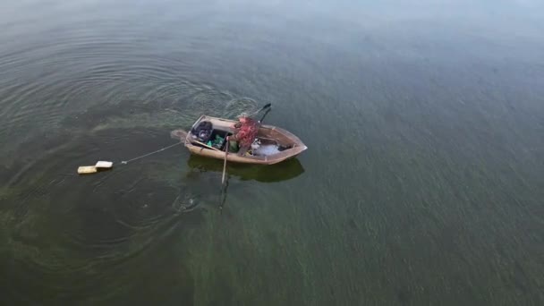 Ένας ψαράς σε μια βάρκα πιάνει ψάρια στη θάλασσα. Πιάνοντας ψάρια του ποταμού από μια βάρκα με κουπιά σε ένα καλάμι ψαρέματος και δίχτυα. Λαθροθηρία. Αθλητική αλιεία στο νερό. — Αρχείο Βίντεο
