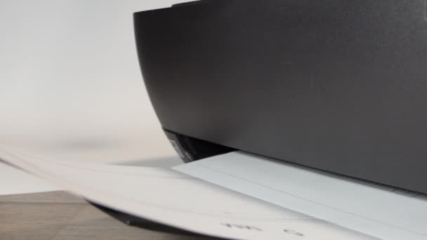 Impresora en acción. Hoja de papel impresa. Detalle plano de impresora negra imprimiendo documentos en ambiente de oficina. 4 k vídeo — Vídeo de stock