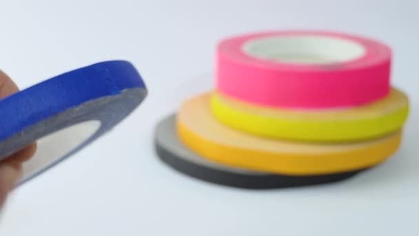 There are many colored teips on the table. A mans hand tears off a piece of blue tape. Colored adhesive tape lies on the table. Blue, yellow, pink, black, orange — Vídeo de Stock