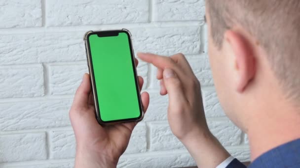 Hombre que utiliza el teléfono inteligente en el espacio de oficina, sentado en la silla y el uso de la maqueta de teléfono de pantalla verde, croma clave, contenido de navegación, video, blogging, tocando el centro de la pantalla, volteando a través de folleto de noticias. — Vídeos de Stock