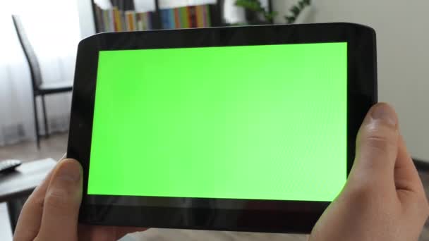 緑の画面のモックアップとタブレットコンピュータを保持する手のクローズアップ。男は部屋の裏に緑色の画面のタブレットを持っています。ビデオ会議用テンプレート. — ストック動画
