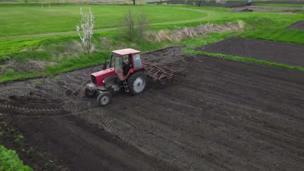 Agricultural red small tractor in the field plowing. System plowing ground on cultivated farm field, pillar of dust trails behind, preparing soil for planting new crop, agriculture concept, top view — стоковое видео