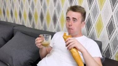 Evde televizyon izleyen gülen ve mutlu yetişkin bir adam. Bir somun ekmek yiyor, kahve içiyor ve televizyon kanallarını değiştiriyor..