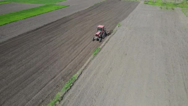 Сельскохозяйственный красный маленький трактор в поле вспашки. Система вспашки почвы на культивируемых сельскохозяйственных полях, столб пылевых троп позади, подготовка почвы для посадки нового урожая, сельскохозяйственная концепция, вид сверху — стоковое видео
