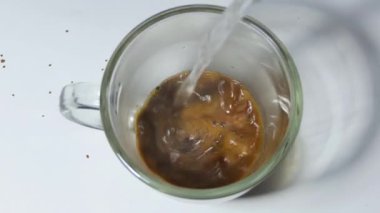 A man brews morning coffee with boiling water close-up. An overhead view of a mug of instant coffee standing on a white table into which a stream of hot water begins to flow.